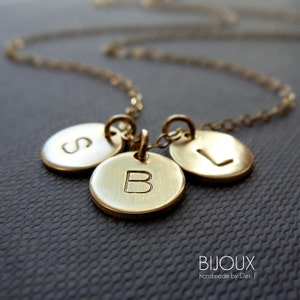 May include: Gold necklace with three round charms, each with a different letter engraved on it. The letters are S, B, and L.