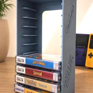 Peut inclure: Un support de rangement vertical bleu clair pour cartouches de jeux vidéo avec le texte Nintendo et Game Boy Advance en relief sur le côté. Le support contient quatre boîtiers de jeux dont Rayman et Pokemon Version Or et Version Jaune.