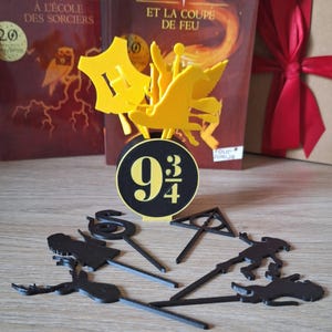 Peut inclure: Ensemble de décorations sur le thème d'Harry Potter en noir et jaune. Comprend un blason jaune de Poudlard, un panneau noir et jaune 9 3/4, et diverses découpes de personnages et de symboles noirs. Des livres avec des titres français sont en arrière-plan.