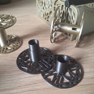 May include: Two black plastic spools with intricate geometric designs, and one gold spool with a similar design. The spools are used for holding thread or yarn.