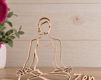 Könnte beinhalten: Eine hellfarbene Skulptur aus dünnen Linien, die eine Person in einer sitzenden Yoga-Pose mit gekreuzten Beinen darstellt. Die Figur besteht aus einem durchgehenden, flachen Material. Rechts daneben steht das Wort Zen in passender Schreibschrift.