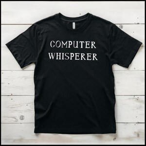 Peut inclure: T-shirt noir avec du texte blanc qui dit "COMPUTER WHISPERER".