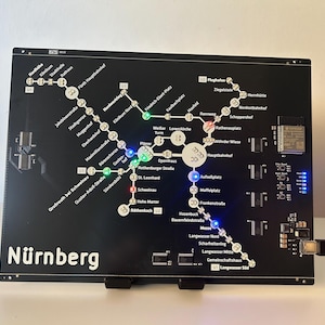 Könnte beinhalten: Eine schwarze Leiterplatte mit einem Plan der Nürnberger U-Bahn. Die Karte zeigt beleuchtete LED-Lichter an den Stationen, mit der Aufschrift "Nürnberg". Ein USB-Kabel ist angeschlossen. Das Board ist auf einem Ständer montiert.