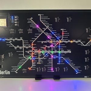 Könnte beinhalten: Schwarz beleuchtete Karte des Berliner U-Bahn-Systems. Die Karte zeigt farbige LED-Leuchten, die die U-Bahn-Linien und -Stationen hervorheben. Das Wort "Berlin" ist unten links in Weiß aufgedruckt.