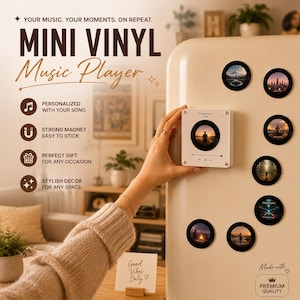 May include: A white square mini vinyl music player with a circular display screen showing a silhouette image, attached to a cream-colored surface. Seven smaller circular black vinyl-style magnets with various landscape images are arranged nearby.