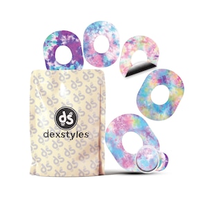 Może przedstawiać: Opakowanie produktów Dexstyles z powtarzającym się wzorem i logo Dexstyles. Kilka plastrów samoprzylepnych z wzorem tie-dye w odcieniach fioletu, niebieskiego, różu i żółtego jest wyświetlanych wokół opakowania. Łaty mają okrągły otwór pośrodku.