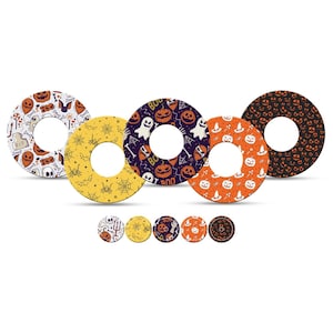 Può includere: Una collezione di decorazioni a forma di ciambella a tema Halloween. I disegni includono zucche, fantasmi e ragni in vari colori come arancione, viola e nero. Sono presenti anche decorazioni circolari più piccole e abbinate.