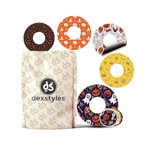 以下が含まれることがあります： ハロウィーンをテーマにした様々なデザインの「dexstyles」製品のパッケージ。デザインには、カボチャ、幽霊、コウモリ、クモの巣が含まれています。製品は中央に穴が開いた円形で、オレンジ、黄色、紫、茶色があります。