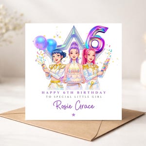 May include: A square birthday greeting card featuring three anime-style characters in white outfits holding party poppers and a cake with candles. Above them is a large iridescent number 6. Text reads: HAPPY 6TH BIRTHDAY TO SPECIAL LITTLE GIRL Rosie Grace.