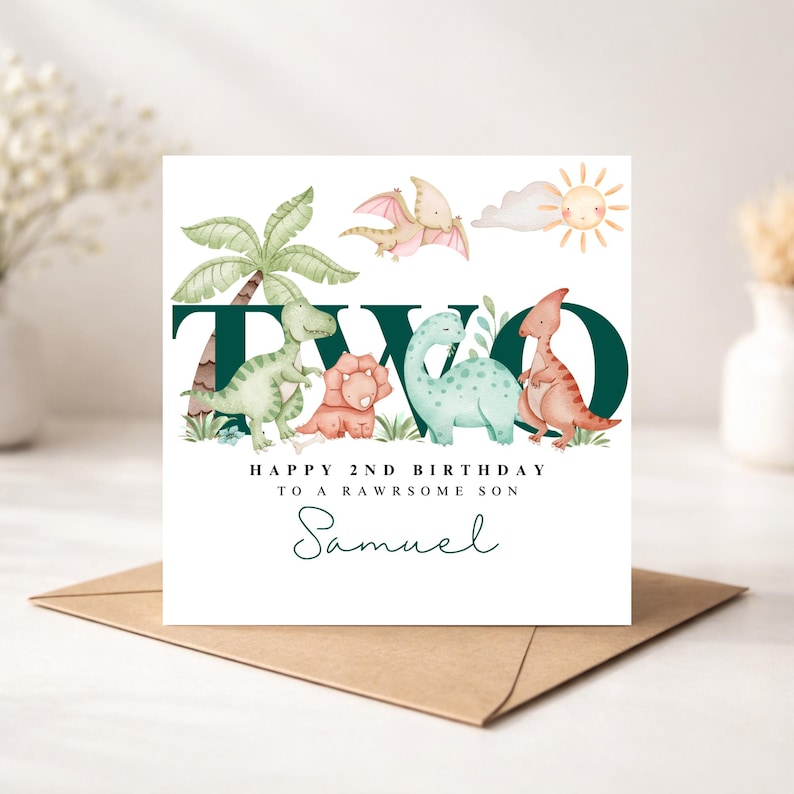May include: A birthday card with a dinosaur theme. The card features the word "TWO" in dark green, with illustrations of dinosaurs, a palm tree, and a sun. The text reads "HAPPY 2ND BIRTHDAY TO A RAWSOME SON" and "Samuel".
