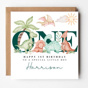 May include: A birthday card with a brown envelope. The card features watercolour illustrations of dinosaurs, a palm tree, and a sun. Text reads "ONE", "Happy 1st Birthday to a special little boy" and a name.