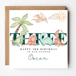 May include: A birthday card with a brown envelope. The card features a watercolour illustration of dinosaurs, a palm tree, and a sun. Text reads "THREE", "HAPPY 3RD BIRTHDAY TO OUR NEPHEW", and "Oscar".