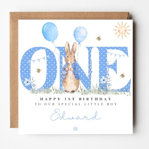 May include: A blue and white birthday card featuring a Peter Rabbit illustration. The card reads "Happy 1st Birthday to our special little boy Edward".