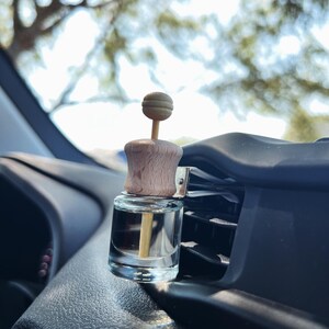 May include: A clear glass bottle with a wooden top and a wooden stick inside. The bottle is attached to a car's air vent.