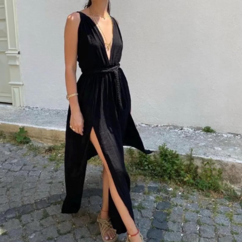 May include: A black maxi dress with a deep V-neckline and a tie at the waist. The dress has a thigh-high slit on the left side.