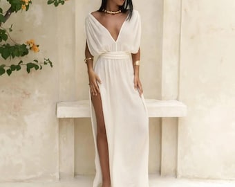 May include: A white maxi dress with a deep V-neckline, short sleeves, and a side slit. The dress has a tie belt at the waist and is made of a lightweight fabric.
