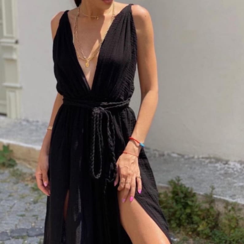 May include: A black maxi dress with a deep V-neckline, a tie at the waist, and a side slit. The dress is made of a soft, flowing fabric.