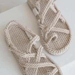 May include: A pair of beige rope sandals. The sandals feature a woven design with a toe loop and straps that crisscross over the foot. The soles are flat and the sandals appear to be made of a natural fiber.