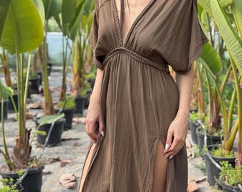 Puede incluir: Un vestido largo de color marrón con un escote en V profundo, mangas cortas estilo kimono y un detalle de trenzado a lo largo del cuello y la cintura. La prenda incluye dos aberturas laterales altas que van desde el muslo hasta el dobladillo.