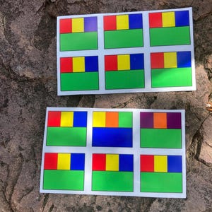 May include: Two sheets of colorful stickers with a repeating pattern of rectangles. Each sticker features a green base, a yellow square, and a red, blue, or purple rectangle above it. The stickers are on a rough, brown stone surface.