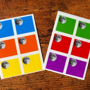Puede incluir: Dos hojas de pegatinas con cuadrados de colores: azul, naranja, amarillo, verde, rojo y morado. Cada cuadrado tiene una imagen detallada de la luna. Las pegatinas están sobre una superficie de madera.