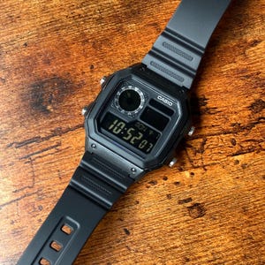 Pu&ograve; includere: Un orologio digitale Casio nero con un cinturino in resina nera. Il quadrante dell'orologio ha un display digitale che mostra l'ora come 10:52:07. L'orologio ha anche un piccolo quadrante analogico nella parte superiore del quadrante.