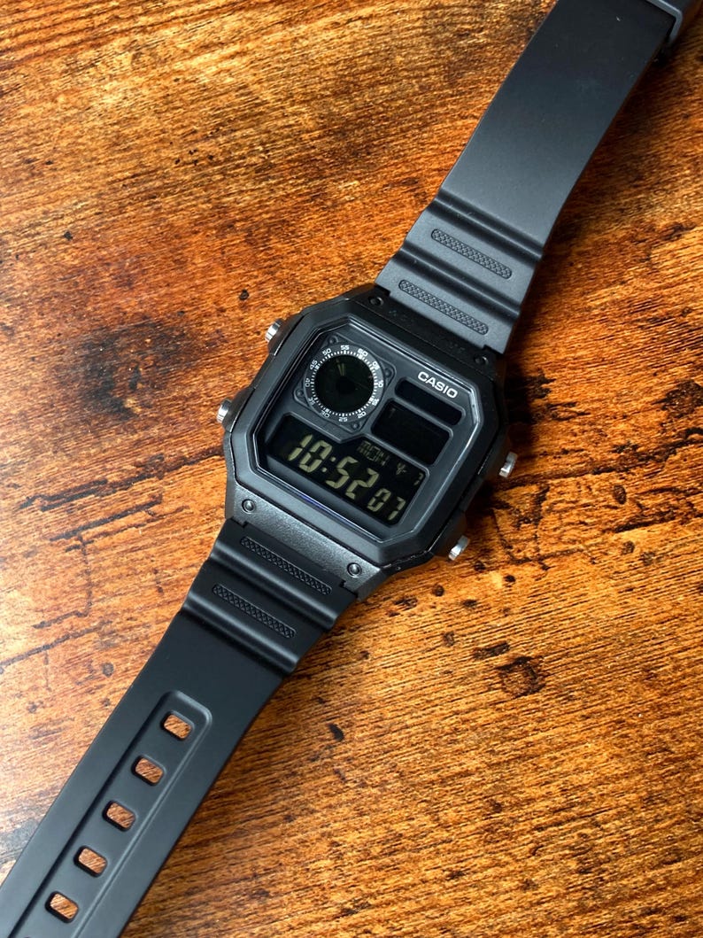 Pu&ograve; includere: Un orologio digitale Casio nero con un cinturino in resina nera. Il quadrante dell'orologio ha un display digitale che mostra l'ora come 10:52:07. L'orologio ha anche un piccolo quadrante analogico nella parte superiore del quadrante.