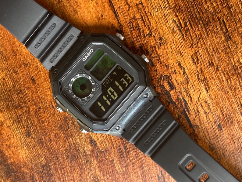Pu&ograve; includere: Un orologio digitale Casio nero con quadrante quadrato e cinturino in resina nera. Il quadrante dell'orologio mostra l'ora, la data e il giorno della settimana. L'orologio ha una retroilluminazione verde.