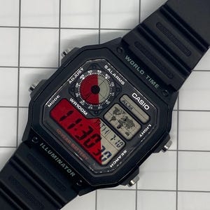 Pu&ograve; includere: Un orologio digitale Casio nero con un display rosso e bianco. L'orologio ha un cinturino in resina nera e un quadrante nero con pi&ugrave; pulsanti. Il quadrante dell'orologio mostra l'ora, la data e il giorno della settimana. L'orologio ha anche una funzione di ora mondiale, una sveglia e un cronometro.
