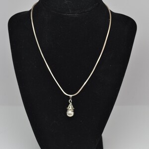May include: A silver chain necklace with a silver pendant featuring a round pearl-like bead with a decorative filigree design.