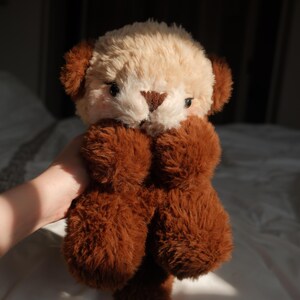 Puede incluir: Un peluche con un dise&ntilde;o de dos tonos que presenta una cabeza de color crema y orejas, brazos y cuerpo de color marr&oacute;n oscuro. El juguete tiene ojos peque&ntilde;os y oscuros, una nariz triangular marr&oacute;n y una textura de pelaje suave y peludo.