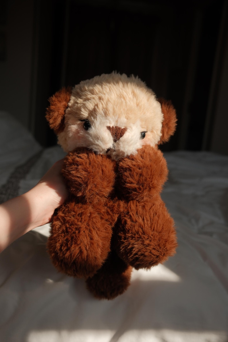 Puede incluir: Un peluche con un dise&ntilde;o de dos tonos que presenta una cabeza de color crema y orejas, brazos y cuerpo de color marr&oacute;n oscuro. El juguete tiene ojos peque&ntilde;os y oscuros, una nariz triangular marr&oacute;n y una textura de pelaje suave y peludo.