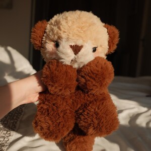 Puede incluir: Un peluche con cara de color crema, nariz triangular de color marr&oacute;n oscuro y orejas de color marr&oacute;n oscuro. El cuerpo, los brazos y las piernas est&aacute;n cubiertos de una piel sint&eacute;tica texturizada de color marr&oacute;n oscuro y denso.