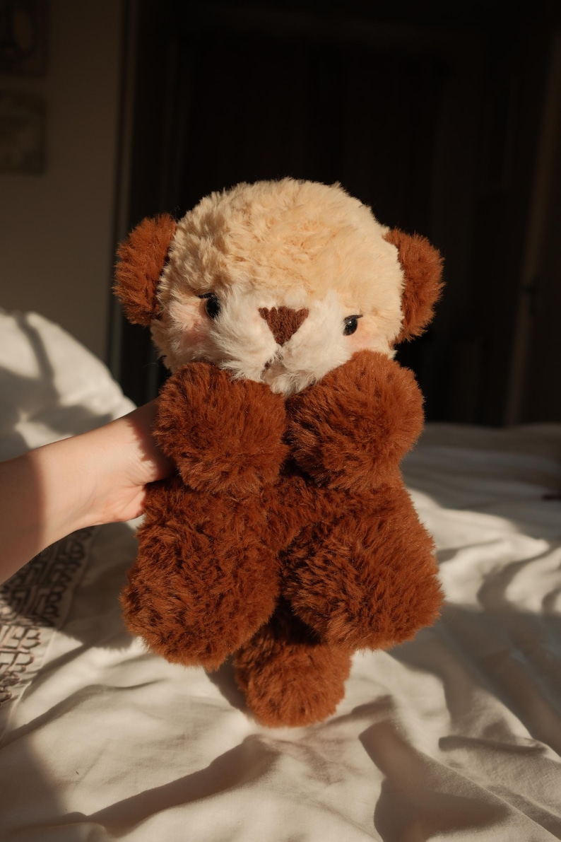 Puede incluir: Un peluche con cara de color crema, nariz triangular de color marr&oacute;n oscuro y orejas de color marr&oacute;n oscuro. El cuerpo, los brazos y las piernas est&aacute;n cubiertos de una piel sint&eacute;tica texturizada de color marr&oacute;n oscuro y denso.