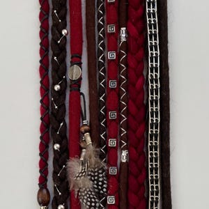 Puede incluir: Un conjunto de rastas sintéticas rojas y marrones con cuentas y abalorios plateados. Las rastas están trenzadas y tienen diferentes texturas.