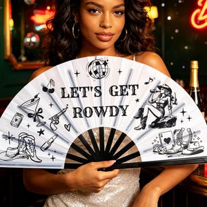 Puede incluir: Un abanico plegable blanco con ilustraciones negras que incluyen una bola de discoteca, botas de vaquero, un sombrero, una copa de martini y el texto "LET'S GET ROWDY" en negrita. El abanico tiene varillas negras e iconos de estilo vaquero.