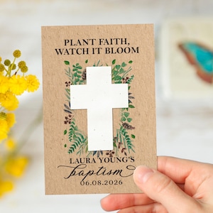 Puede incluir: Tarjeta de anuncio de bautizo con el texto "PLANT FAITH, WATCH IT BLOOM" y un diseño de cruz blanca. La tarjeta está decorada con vegetación de acuarela, el nombre "LAURA YOUNG'S" y la fecha "06.08.2026".