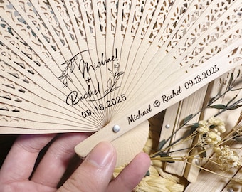 Op de afbeelding: Een houten handwaaier met een decoratief uitgesneden ontwerp. De waaier is gepersonaliseerd met de namen "Michael & Rachel" en de datum "09.18.2025".
