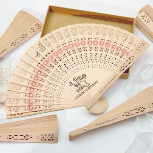 May include: Wooden fans with intricate cut-out designs and floral patterns in red. The central fan features the text "A Tiny Bit Older, Lauren's Birthday". Several fans are displayed, some open and some closed, with a gift box.