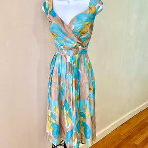 Puede incluir: Vestido sin mangas con escote en V y falda a la rodilla. El vestido presenta un estampado floral en tonos azules, amarillos y marrones. El vestido se exhibe en un maniqu&iacute; blanco. El vestido tiene cintura entallada y falda plisada.