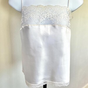 Pu&ograve; includere: Una camisole di raso bianco con delicate finiture in pizzo sullo scollo e sull'orlo. La camisole ha sottili spalline e un design semplice ed elegante. I dettagli in pizzo aggiungono un tocco di fascino vintage.
