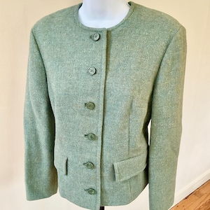 May include: A light green blazer with a round neckline and button-up closure. The blazer has two front pockets and is displayed on a white mannequin. The fabric has a textured appearance.