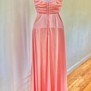 May include: A peach-colored formal gown with a halter neckline and a floor-length skirt. The bodice features a ruched design, and the dress is displayed on a white mannequin. The dress has a zipper closure down the back.