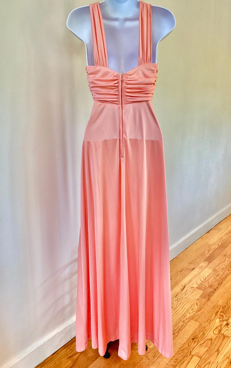 May include: A peach-colored formal gown with a halter neckline and a floor-length skirt. The bodice features a ruched design, and the dress is displayed on a white mannequin. The dress has a zipper closure down the back.