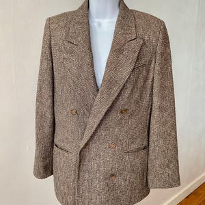 May include: A double-breasted blazer in a textured brown and tan tweed fabric. The garment features wide notched lapels, long sleeves, two front flap pockets, and four visible brown buttons arranged in a two-by-two pattern on the front.