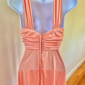 May include: A peach-colored vintage dress with a halter neckline and a flowing skirt. The dress features a ruched bodice and a zipper closure down the back. The dress is displayed on a mannequin.