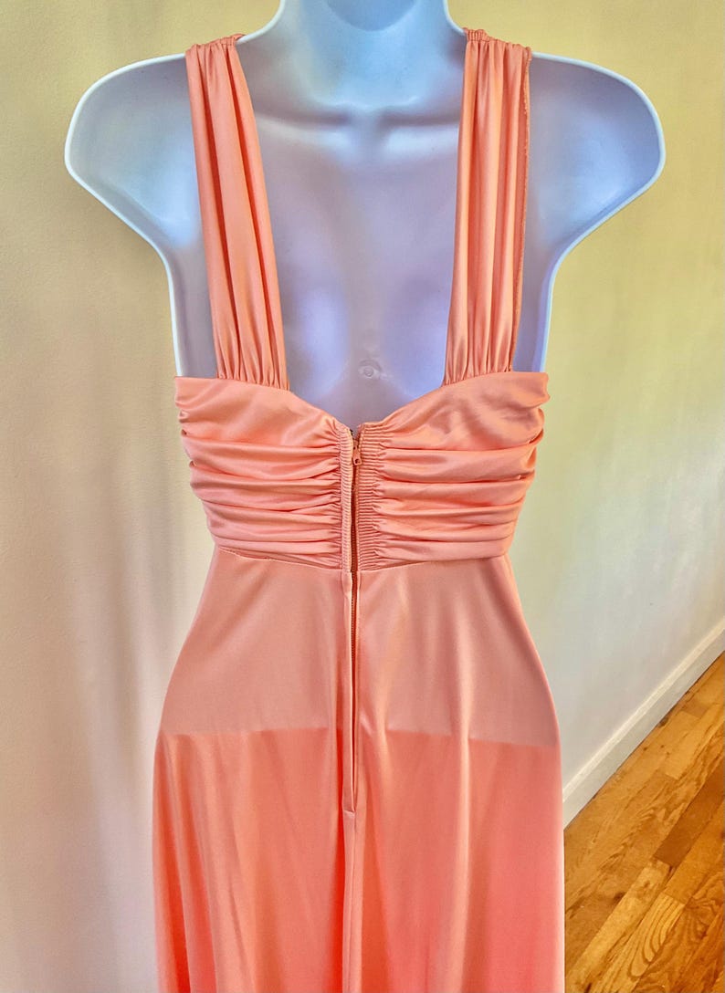 May include: A peach-colored vintage dress with a halter neckline and a flowing skirt. The dress features a ruched bodice and a zipper closure down the back. The dress is displayed on a mannequin.