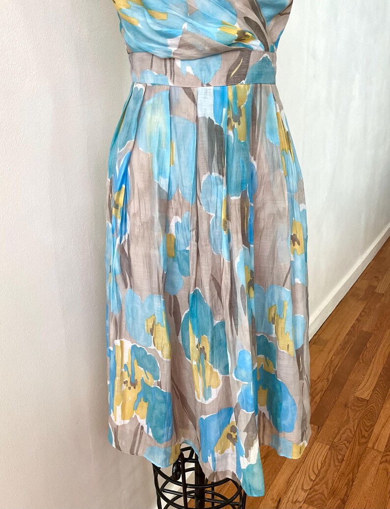 Puede incluir: Vestido sin mangas con estampado floral en tonos azules, amarillos y marrones. El vestido tiene un corpi&ntilde;o ajustado y una falda plisada. La tela parece ligera, adecuada para climas c&aacute;lidos. Aproximadamente 100 cm de largo.
