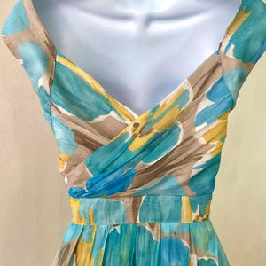 Puede incluir: Vestido de verano sin mangas con estampado floral en tonos azul, amarillo y marr&oacute;n. El vestido presenta un escote en V y una cintura entallada. La tela parece ligera y fluida, ideal para el clima c&aacute;lido.