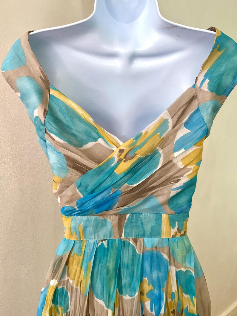 Puede incluir: Vestido de verano sin mangas con estampado floral en tonos azul, amarillo y marr&oacute;n. El vestido presenta un escote en V y una cintura entallada. La tela parece ligera y fluida, ideal para el clima c&aacute;lido.
